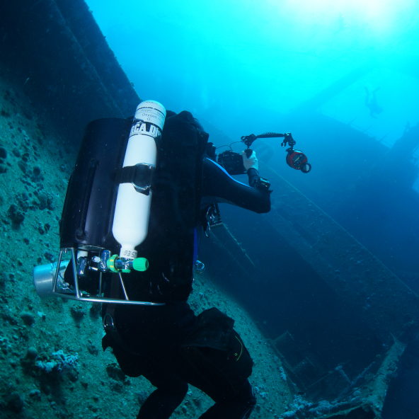 A diver with a rebreather taking a photo of a ship wreck